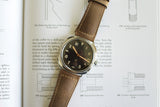 Luxury wristwatch with brown leather strap and black dial on an open technical book