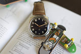 Luxury watch with brown leather strap on a book, beside two mini skateboards