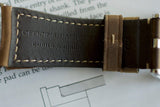 Close-up of brown stitched leather watch strap with engraved text and silver buckle