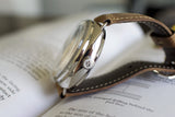 Close-up of a luxury stainless steel watch with brown leather strap resting on an open book