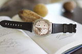 Luxury Swiss watch with visible mechanical movement and black leather strap on open book