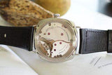 Luxury Swiss watch with open caseback and black leather strap on white surface