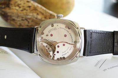 Luxury Swiss watch with open caseback and black leather strap on white surface