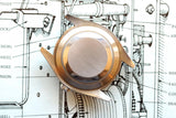 Stainless steel luxury watch case back resting on a technical watch blueprint.
