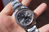 Close-up of a silver Rolex Datejust luxury watch with a dark dial and diamond markers on a hand