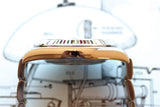 Close-up side profile of a gold luxury Swiss watch against a technical blueprint background