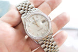 Close-up of a Rolex Datejust luxury watch with diamond bezel and bracelet held in a hand.