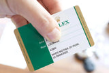 A hand holding a Rolex international guarantee card for a white mother-of-pearl diamond watch.