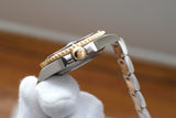 Close-up side view of a luxury gold and steel watch held by a gloved hand.