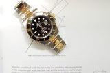 Two-tone Rolex Submariner Date luxury watch with black bezel and gold accents on white paper