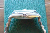 Side profile of a luxury Swiss-made wristwatch with a metal link bracelet on a green textured surface