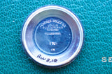 Close-up of a Rolex stainless steel watch case back with engravings on a green textured background