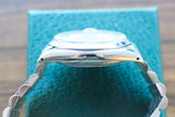 Side profile of a luxury silver Swiss watch with a metal bracelet on a blue box