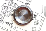 Stainless steel Rolex watch case back resting on a technical drawing.
