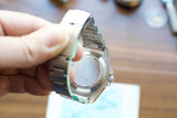 Close-up of a person holding a luxury Swiss-made watch showing the case back and metal bracelet
