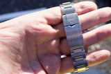 Close-up of a luxury stainless steel watch bracelet held in a hand, showing a crown logo.