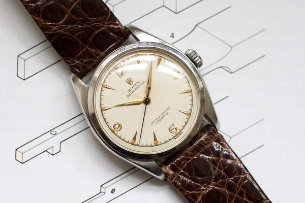 Vintage luxury stainless steel watch with cream dial and brown leather strap on paper background