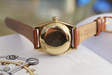 Vintage gold watch with brown leather strap, caseback view on open book
