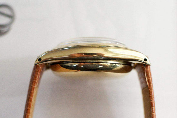 Side view of vintage gold watch case with brown leather strap on white background