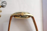 Side view of vintage gold Swiss watch with leather strap on a light surface