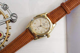 Vintage gold luxury watch with textured brown leather strap on open book
