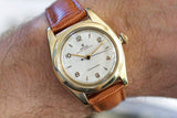 Vintage gold Rolex Bubbleback wristwatch with brown leather strap on wrist