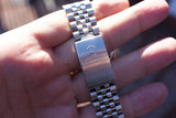 Close-up of a stainless steel Rolex luxury watch bracelet clasp held in a hand.