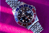 Close-up of a Rolex GMT-Master II luxury watch with a blue and red bezel on a steel bracelet.