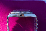 Side view of a luxury Swiss dive watch with a silver metal bracelet on a purple background