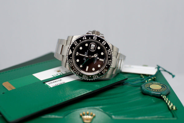 Stainless steel GMT watch with black bezel on green display box and certification cards