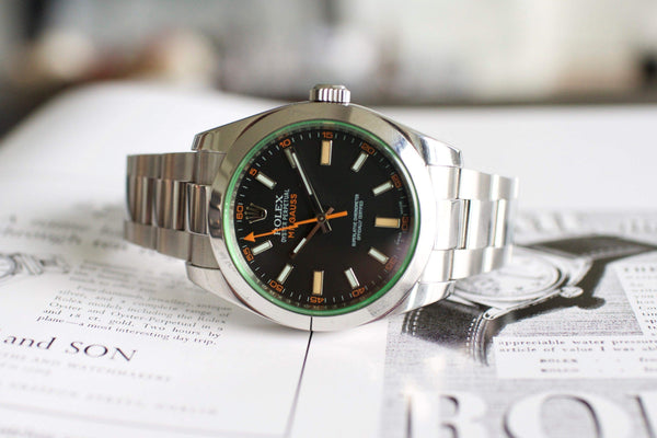 Stainless steel luxury watch with black dial, green sapphire crystal, and orange accents
