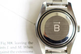 Close-up of stainless steel luxury watch case back with engraved arrow and letter B symbol