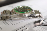 Close-up of luxury stainless steel Swiss watch with green bezel and black dial on paper