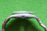 Side view of a luxury silver-tone stainless steel wristwatch on a green background.