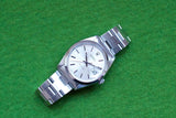 Vintage Rolex Oyster Perpetual silver watch with stainless steel bracelet on green background