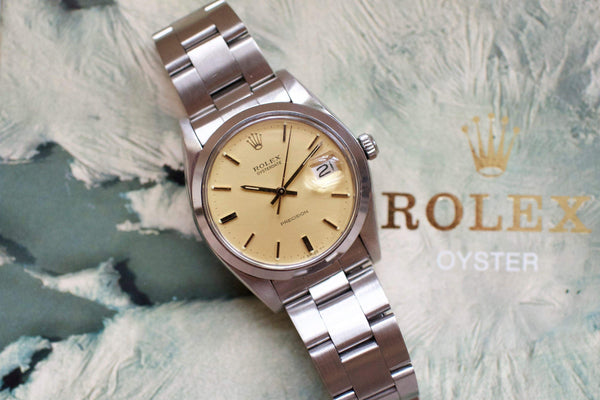 Vintage stainless steel Rolex watch with cream dial and date display on textured background