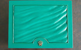 Green luxury watch box with gold crown emblem, textured lid, centered on dark surface