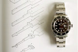 Stainless steel luxury diver watch with black dial and rotating bezel on technical drawing background