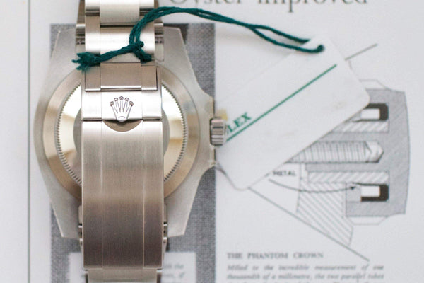 Close-up of a stainless steel luxury watch clasp with logo, green tag, and authentication card