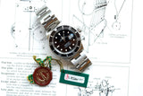 Rolex Submariner luxury watch with certification tag on vintage clock blueprints
