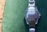 Rear view of a stainless steel luxury Swiss watch case and bracelet on a green surface