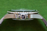 Side view of a luxury Swiss watch with a crown logo and rotating bezel on a green background
