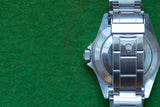 Back view of a silver luxury Swiss watch with metal bracelet on a green felt background