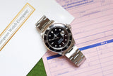 Rolex Submariner luxury watch with black dial and silver oyster bracelet on pink paperwork