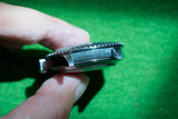 Close-up side view of a luxury stainless steel dive watch held against a green background