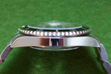 Side view of a luxury stainless steel dive watch with a rotating bezel on a green background