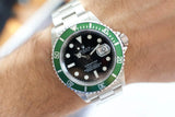 Stainless steel luxury watch with green bezel and black dial on wrist, date magnifier visible