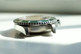 Close-up of stainless steel luxury dive watch case with green bezel and engraved details