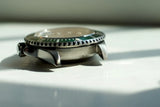 Close-up of a luxury stainless steel watch case with green bezel and engraved reference number