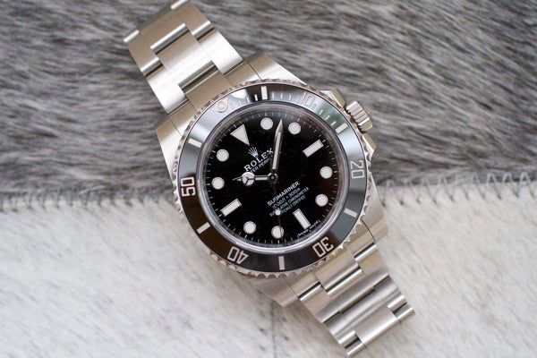Stainless steel luxury dive watch with black bezel and black dial on a textured surface